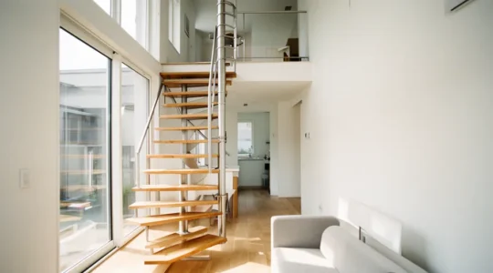 Vue intérieure d'une maison à étage moderne avec escalier hélicoïdal compact en métal et bois, salon lumineux au rez-de-chaussée