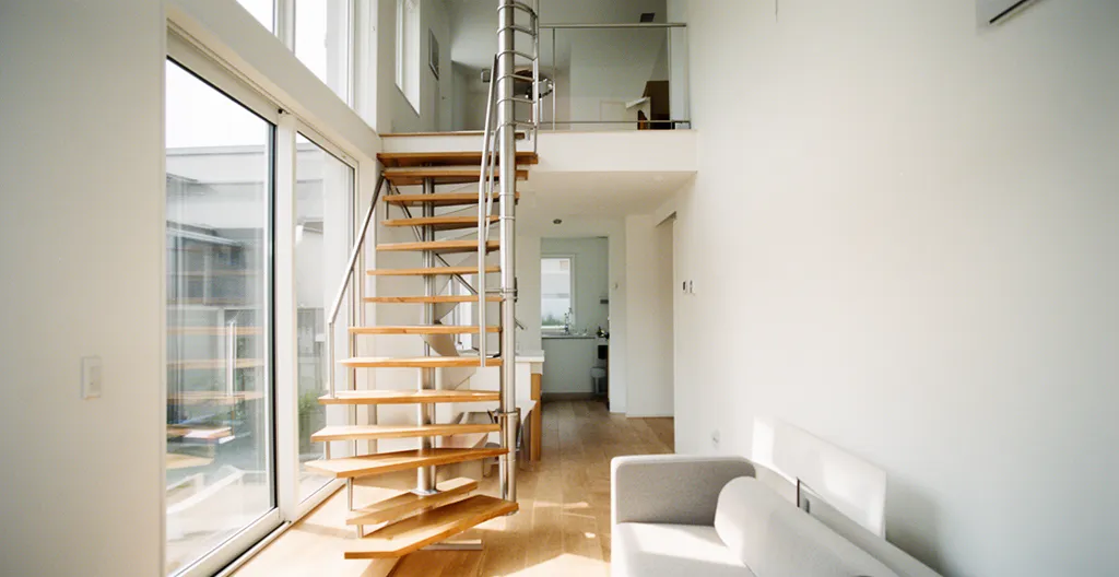 Vue intérieure d'une maison à étage moderne avec escalier hélicoïdal compact en métal et bois, salon lumineux au rez-de-chaussée